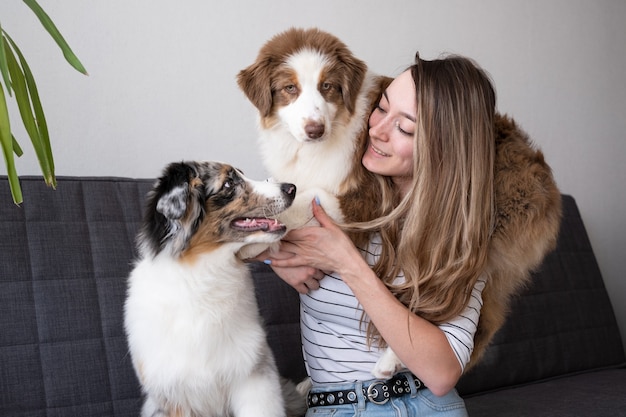 Attractive happy woman holding two beatiful Small cute Australian shepherd blue merle puppy dog. Red three colours. Love and friendship between human and animal.