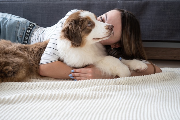 魅力的な幸せな女性のキス小さなかわいいオーストラリアンシェパードの赤い3色の子犬の犬。