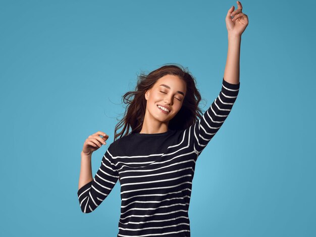 Attractive happy woman with beautiful fly hair in stripes hands up dancing color background