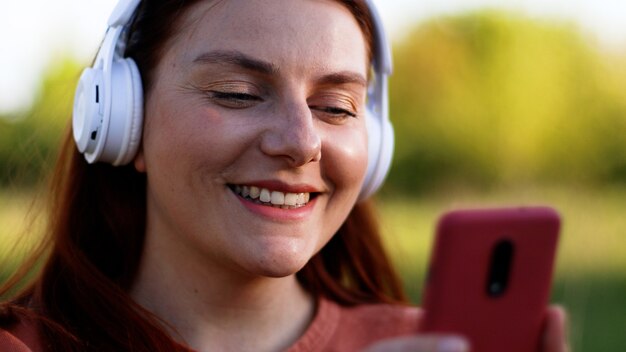 ヘッドフォンで音楽を聴いている魅力的な幸せな若い女の子の学生。携帯電話のチャットを使用している学生。