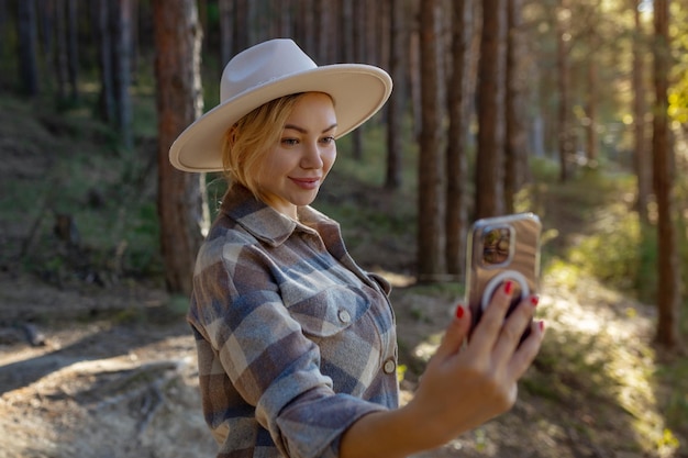 Photo attractive happy young hipster woman wearing a stylish hat in a fashionable one stands in the park