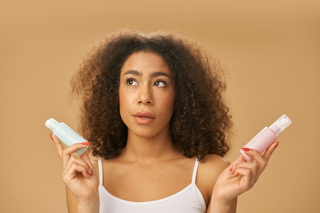 Attractive healthy african american young woman looking doubtful while choosing between two beauty