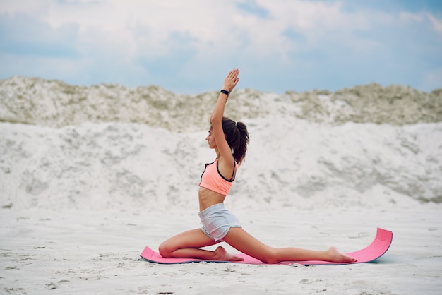 Attractive and healthy young woman doing exercises on the beach at sunrise