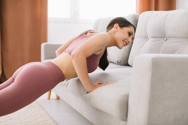 Foto giovane donna attraente e in buona salute che fa flessioni sul divano mentre si riposa a casa