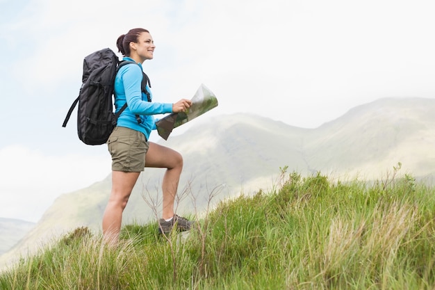 Attractive hiker with backpack hiking uphill holding a map