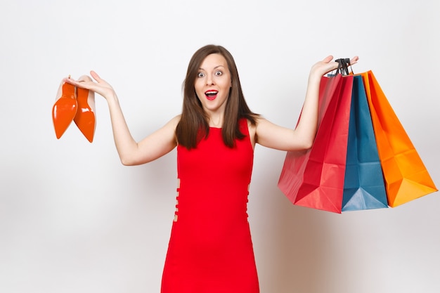 Attractive impressive glamour caucasian fashionable young brown-hair woman in red dress holding beige shoes with red sole, multi colored packets with purchases, shopping isolated on white background.