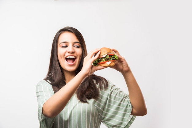 Attraente ragazza asiatica indiana che mangia hamburger su sfondo bianco o giallo