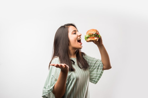 Привлекательная индийская азиатская девушка ест гамбургер на белом или желтом фоне