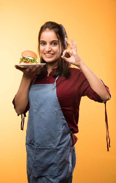 Привлекательная индийская азиатская девушка ест гамбургер на белом или желтом фоне