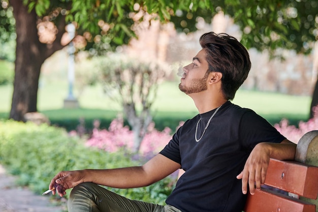 Attractive indian man smoker exhales cigarette smoke portrait in black t shirt and silver neck chain