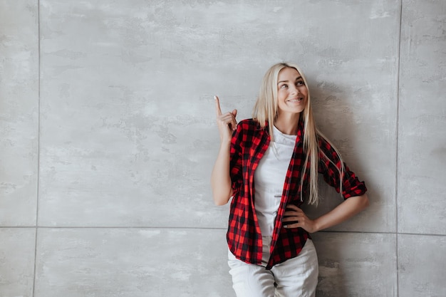Attractive italian blonde woman in plaid shirt pointing aside\
at empty space against marble wall