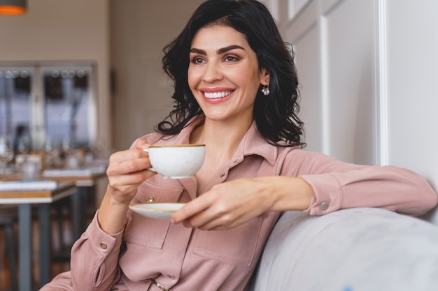 一杯のコーヒーとソーサーを持って目をそらして笑っている魅力的な女性