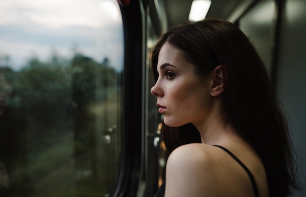 Привлекательная дама смотрит в окно поезда с задумчивым лицом на красивый вечерний пейзаж
