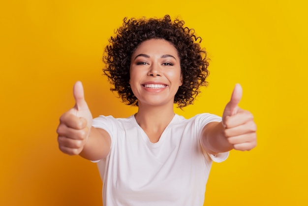 Attractive lady raise two thumbs up shiny white smile on yellow wall