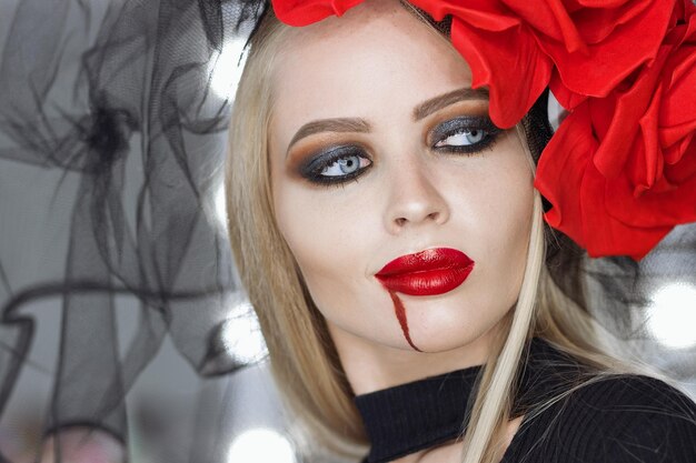 Attractive lady with spill of blood near lips smirking and looking at camera while wearing Gothic