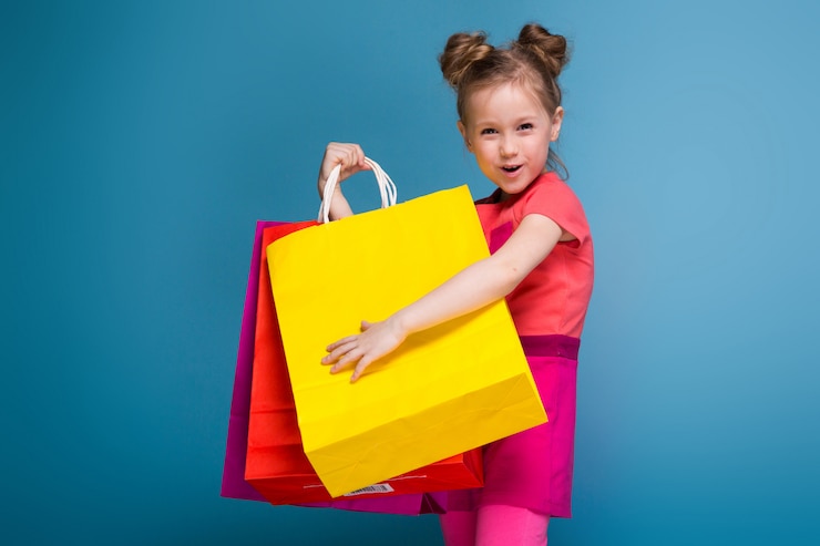 Photo attractive little cute girl in pink dress holds purple paper bag