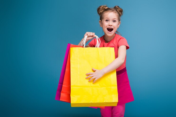 Photo attractive little cute girl in pink dress holds purple paper bag