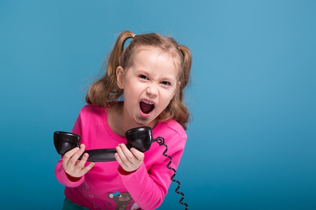 Attraente bambina carina in camicia rosa con scimmia e pantaloni blu parla un telefono