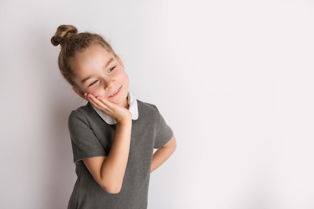 Attractive little girl in a strict school dress, stands on a white background, gestures with her hands, admires a happy expression on her face. High quality photo