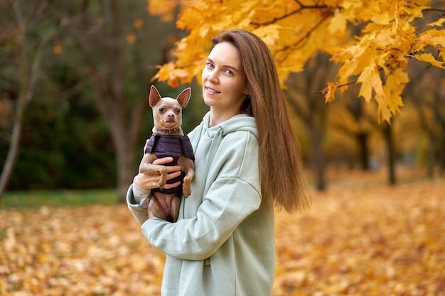 写真 秋の公園でポーズをとっている彼女の犬のおもちゃのテリアと魅力的な長髪のウォーワン