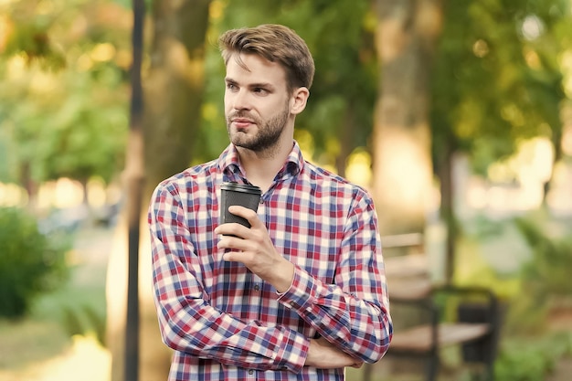 attractive macho man hold hot paper cup with takeout tea or coffee beverage wearing casual plaid checkered shirt outdoor morning energy