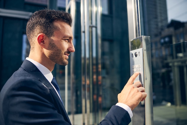 Attractive male with designer beard staying outside business center while trying to press button