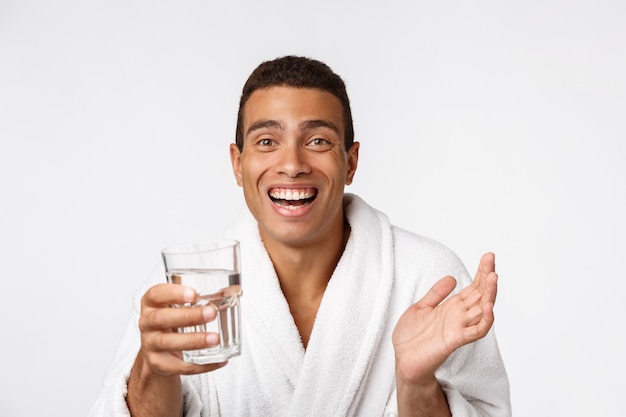 An attractive man drinking a glass of water against white