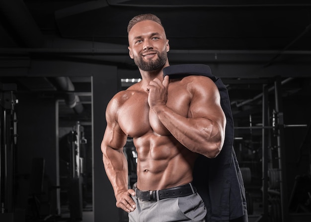 Attractive man in gray pants posing in the gym. Business and bodybuilding concept. Sports activities. Mixed media