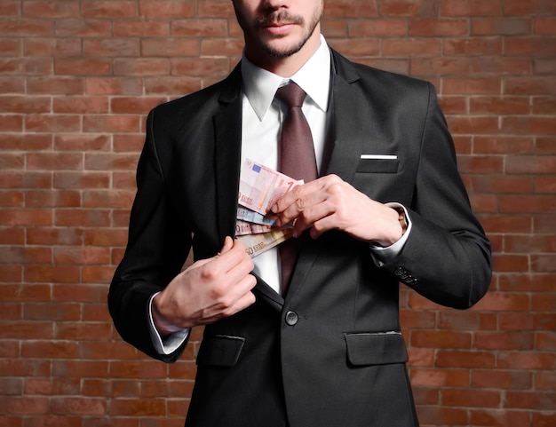 Attractive man hiding euro banknotes in suit on brick wall background