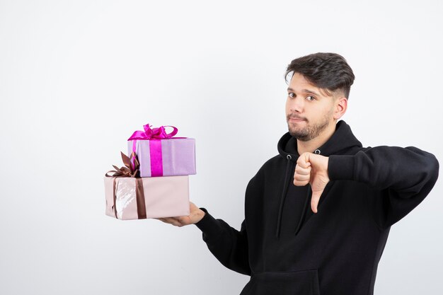 Attractive man holding two present boxes and showing thumb down 