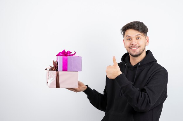 Attractive man holding two present boxes and showing thumb up