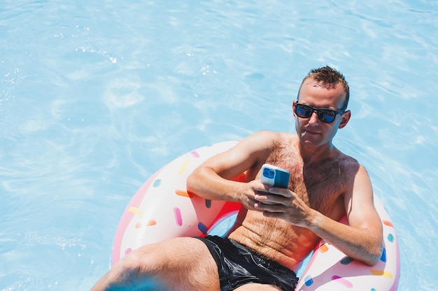 매력적인 남자가 수영장에 있는 풍선 링 위에서 휴식을 취하고 있다 수영장에 있는 남자가 전화 휴가와 자유 시간 개념에 대해 이야기하고 있다