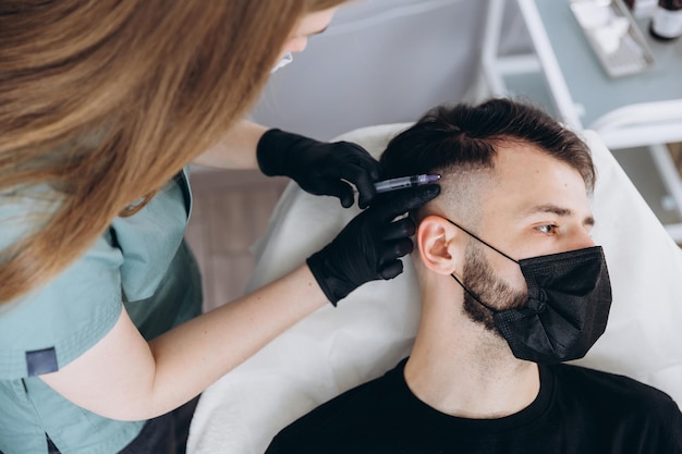 An attractive man receives mesotherapy injections to treat hair loss at the clinic injections into the skin and scalp