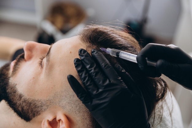 Un uomo attraente riceve iniezioni di mesoterapia per curare la caduta dei capelli presso la clinica iniezioni nella pelle e nel cuoio capelluto