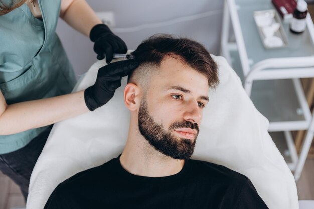 An attractive man receives mesotherapy injections to treat hair loss at the clinic Injections into the skin and scalp