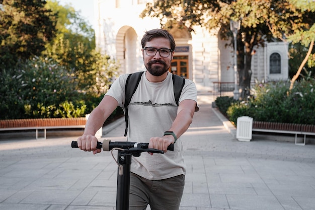 Attractive man riding a kick scooter at cityscape background