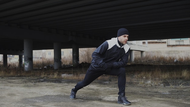 Attractive man runner doing stretching exercise for morning workout and jogging at urban location