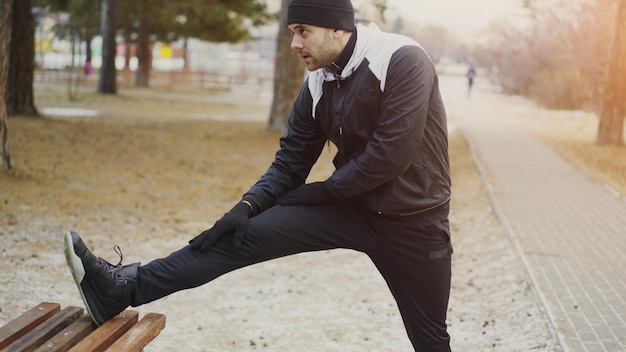 Foto attraente corridore uomo che fa esercizio di stretching preparandosi per l'allenamento mattutino e fare jogging