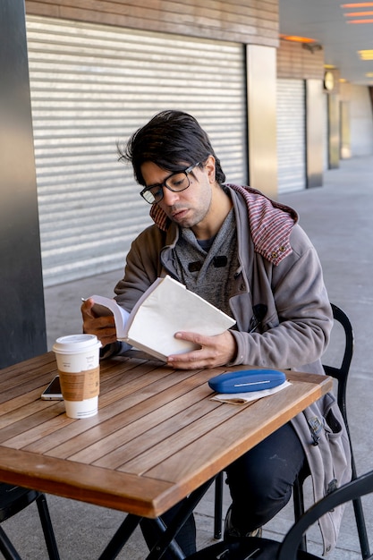 Uomo attraente seduto in un bar a bere caffè mentre legge un libro. orientamento verticale