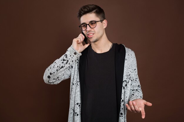 Attractive man standing on brown isolated background and talking per mobile phone.