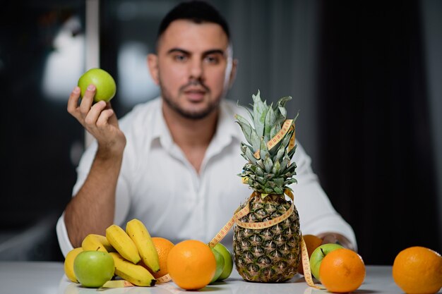 新鮮な果物があるテーブルに座って彼の手にリンゴを持つ魅力的な男