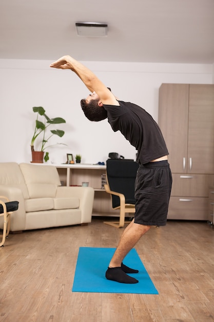 Attractive man with beard doing back stretch standing up. Adult working out.