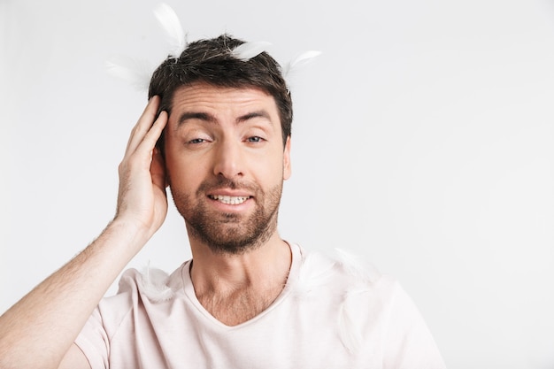 attractive man with bristle in casual t-shirt standing under falling feathers isolated over white wall