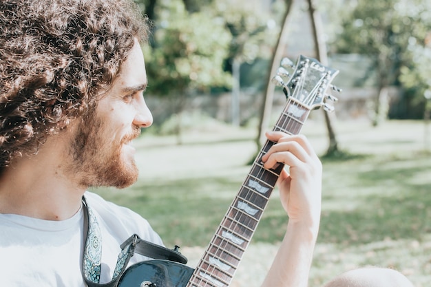 Attractive man with long hair playing acoustic guitar outdoors, hippie, relax, park lifestyle, hobby, copy space