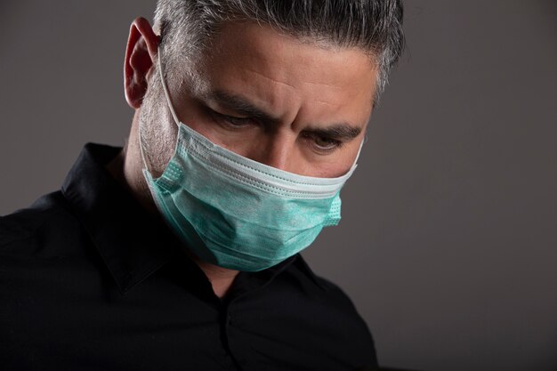 灰色の背景に手術用保護マスクを持つ魅力的な男。コロナウイルスの概念。健康を守ります。