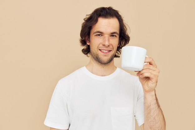 Attractive man with a white mug in his hands emotions posing beige background