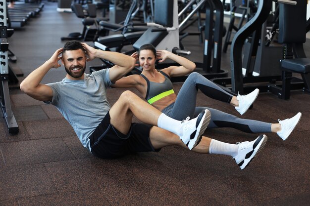 매력적인 남자와 여자는 체육관에서 윗몸 일으키기를 수행하는 쌍으로 작업합니다.