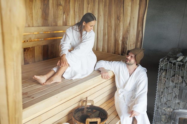 Attractive man and young woman resting in wooden sauna