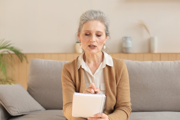 Attractive mature woman sitting on the couch and making notes in diary.