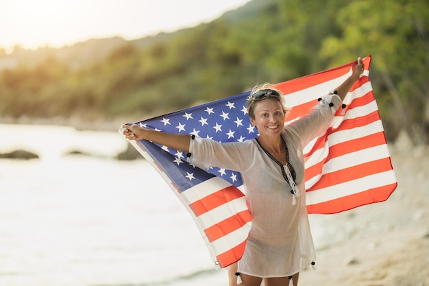 ビーチでリラックスした一日を楽しんでいるアメリカ国旗を持つ魅力的な中年女性。